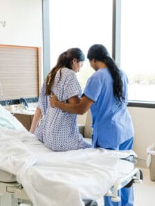 Woman nurse helping her woman patient get up from bed